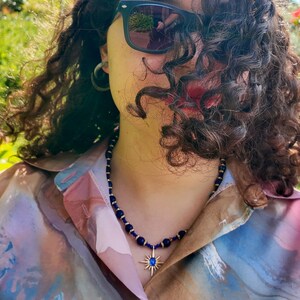 Daylight side view: the blue strand crosses the collarbone in an even rhythm of round beads and gold rondelles, the starburst pendant hanging just above the open shirt.