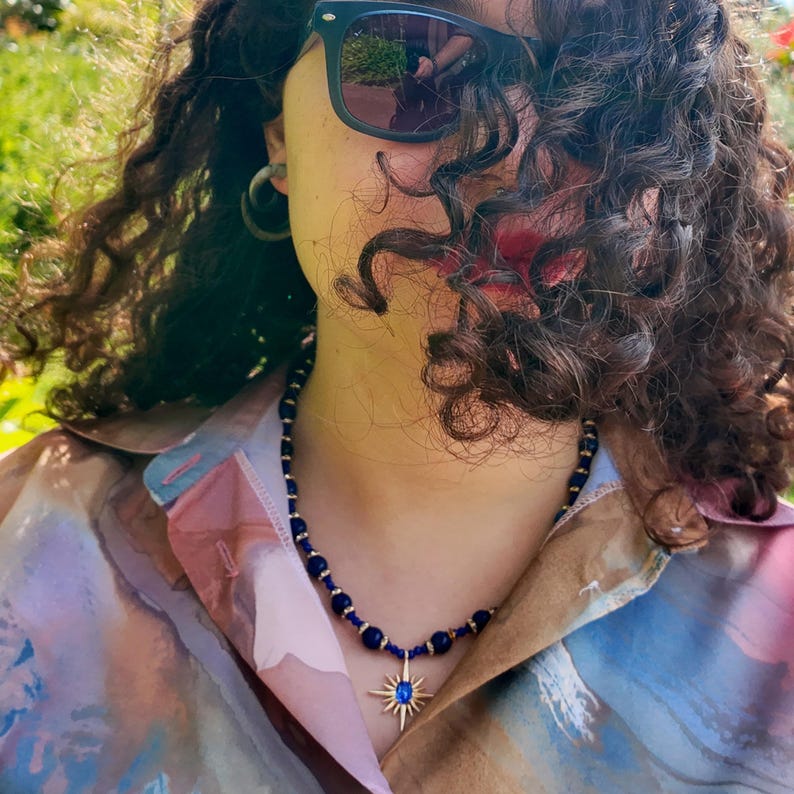 Daylight side view: the blue strand crosses the collarbone in an even rhythm of round beads and gold rondelles, the starburst pendant hanging just above the open shirt.
