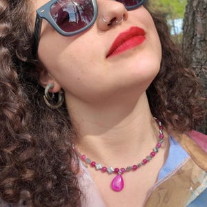 Worn in sunlight, the short strand of bright pink beads and small stamped diamond spacers curves around the base of the neck, the pink teardrop resting just below the hollow of the throat.