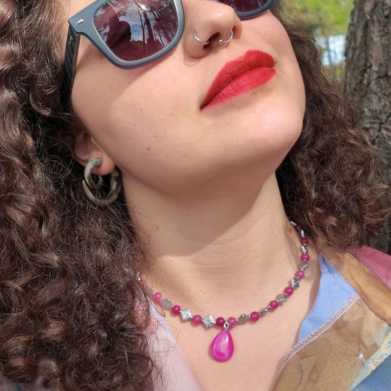 Worn in sunlight, the short strand of bright pink beads and small stamped diamond spacers curves around the base of the neck, the pink teardrop resting just below the hollow of the throat.