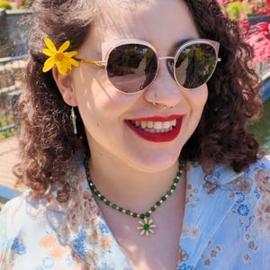 Close daylight view of the necklace — evenly spaced grass-green round beads with tiny gold tubes between them, and a cream-petalled daisy pendant with a green cabochon centre at the front.