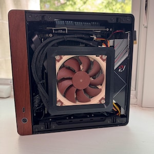 Peut inclure: Un bo&icirc;tier d'ordinateur compact avec un panneau lat&eacute;ral imitation bois. L'int&eacute;rieur comprend un grand ventilateur marron, des c&acirc;bles noirs et une carte m&egrave;re. Le bo&icirc;tier est ouvert, r&eacute;v&eacute;lant les composants internes.