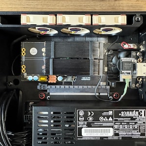 May include: A black computer case interior containing a power supply unit with a label reading Enhance Electronics Co., Ltd., three tan cooling fans, a black circuit board with heat sinks, a PCIe slot, and various black power cables.