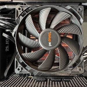 May include: A computer fan with black blades and a copper-colored heat sink. The fan has the brand name "be quiet!" printed on the center. The fan is installed inside a computer case with various wires and components visible.