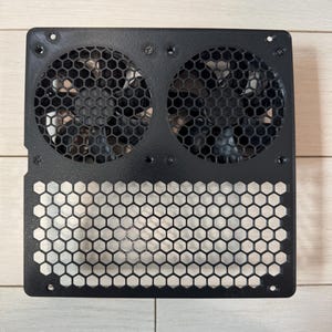 May include: Black metal computer fan housing with two circular fan openings and a honeycomb pattern. The housing has screw holes for mounting. The fans are visible behind the protective grill.