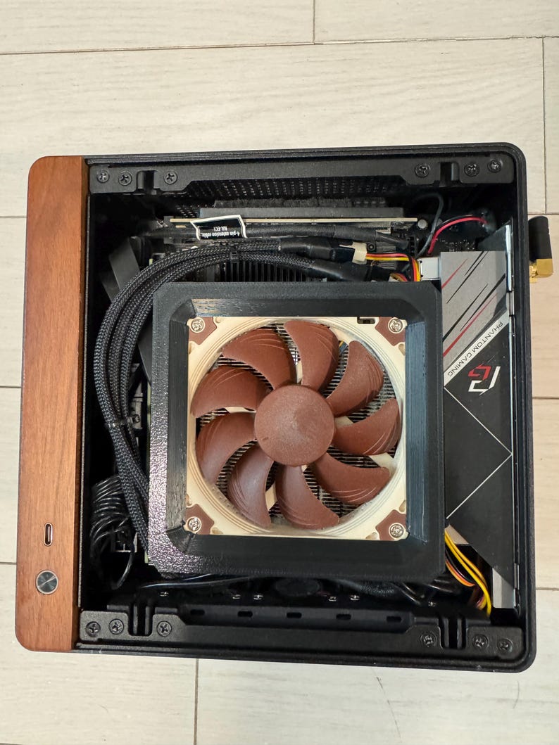 Peut inclure: Un bo&icirc;tier d'ordinateur compact avec un panneau avant en bois. &Agrave; l'int&eacute;rieur, on aper&ccedil;oit un refroidisseur de processeur avec un grand ventilateur marron, une carte graphique et des c&acirc;bles. Le bo&icirc;tier est ouvert, r&eacute;v&eacute;lant les composants internes.