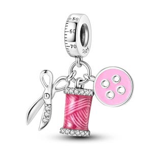 May include: Silver charm with a pink button, spool of thread, and scissors. The charm has a silver measuring tape with numbers 50, 60, and 70. The charm is marked with 925.