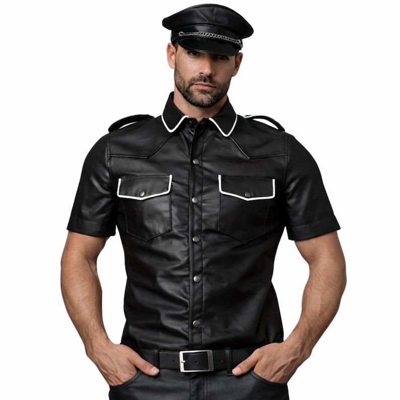 Pode incluir: Camisa preta de couro de manga curta com acabamento branco na gola e nos bolsos. A camisa tem uma frente abotoada e ombreiras. Uma boina de couro preta com corrente prateada tamb&eacute;m &eacute; vis&iacute;vel.