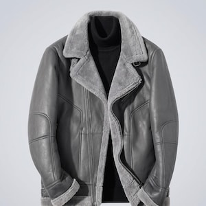 Peut inclure: Veste en cuir grise avec col et doublure en peau de mouton. La veste est dotée d'une fermeture éclair, de plusieurs poches et d'une ceinture à boucle à la taille. Un style classique, adapté au froid.