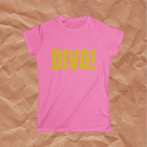 May include: A short-sleeved crew neck t-shirt in a bright pink color. The center of the chest features the word DIVA! printed in a bold, mustard yellow sans-serif font. The garment has a standard fit with a straight hemline and short sleeves.
