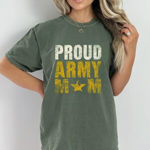 Op de afbeelding: Olijfgroen T-shirt met de tekst "PROUD ARMY M*M" in wit en geel. Het shirt heeft een ronde hals en korte mouwen. De tekst bevat een ster-afbeelding. Het shirt is gemaakt van een zacht, comfortabel materiaal.