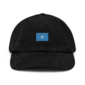 May include: Black corduroy baseball cap featuring a small embroidered flag of Somalia on the front. The flag is a light blue rectangle with a white star in the center. The cap has a curved brim and a structured crown.