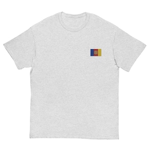 May include: A light gray short-sleeve t-shirt featuring a small, rectangular embroidered patch on the left chest. The patch displays the national flag of Andorra, which consists of vertical blue, yellow, and red stripes with a central coat of arms.