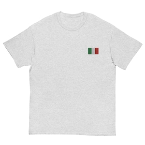 May include: A pale grey t-shirt with a small embroidered Italian flag on the left chest. The flag has green, white, and red vertical stripes. The shirt has short sleeves and a crew neck.