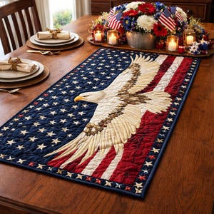May include: A patriotic table runner featuring a detailed embroidered bald eagle with outstretched wings, set against a backdrop of the American flag. The runner is primarily navy blue with white stars and red and white stripes.