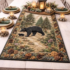 May include: A rectangular table runner with a forest scene featuring a black bear and cub. The runner has a detailed border of pine cones and foliage. Candles and place settings surround the runner.