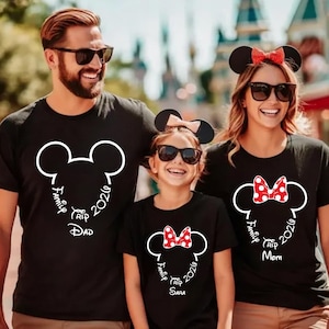 K&ouml;nnte beinhalten: Drei Personen tragen passende schwarze T-Shirts mit einem wei&szlig;en Mickey Mouse-Kopf-Design. Die Shirts tragen die Aufschrift "Family Trip 2026" und die W&ouml;rter "Dad", "Mom" und "Sara" unter dem Design. Die Familie tr&auml;gt Sonnenbrillen und M&auml;useohren.