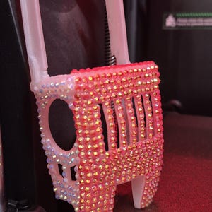 May include: A 3D printer component, adorned with numerous iridescent rhinestones. The component is primarily pink with a white base and accents. The rhinestones create a sparkling effect, enhancing the aesthetic of the 3D printer.