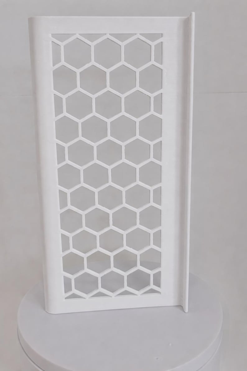 May include: A white, rectangular, upright panel featuring a repeating honeycomb or hexagonal cutout pattern. The structure has a smooth, solid border frame and a flat, vertical edge on the right side, presenting a clean, geometric design.