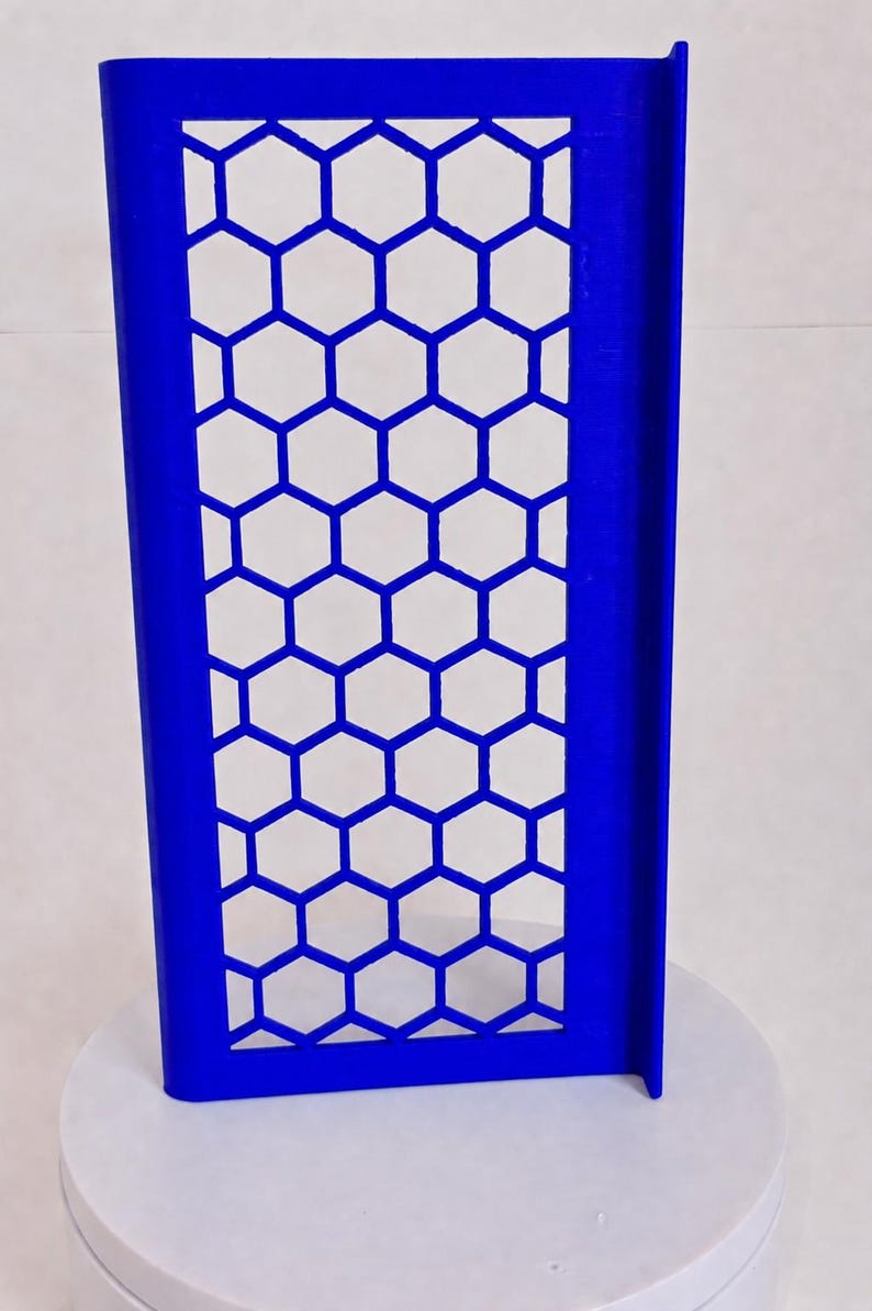 May include: A rectangular blue panel featuring a repeating honeycomb pattern of hexagonal cutouts. The panel has a solid frame and a perpendicular side flange, standing upright on a circular base. The structure is uniform in color and design.