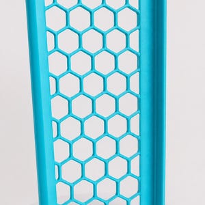 May include: A bright cyan rectangular panel featuring a repeating hexagonal honeycomb grid pattern. The structure is framed by solid vertical borders on the left and right sides, creating a rigid, open-work design with a matte finish throughout.