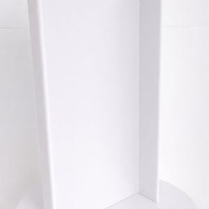 May include: A tall, solid white display stand featuring a vertical rectangular panel attached to a circular base. The structure is constructed with a smooth, matte finish and a clean, uniform white color throughout the entire object.