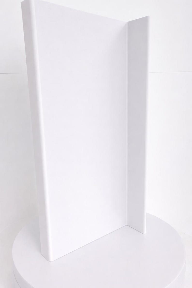 May include: A tall, solid white display stand featuring a vertical rectangular panel attached to a circular base. The structure is constructed with a smooth, matte finish and a clean, uniform white color throughout the entire object.