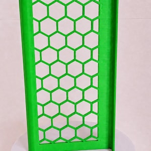 May include: A bright green rectangular panel featuring a repeating honeycomb pattern of hexagonal cutouts. The panel has a solid vertical border on the left and a perpendicular flange extending along the right edge, creating an L-shaped profile.