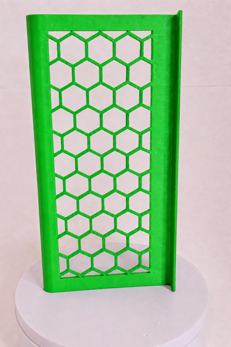 May include: A bright green rectangular panel featuring a repeating honeycomb pattern of hexagonal cutouts. The panel has a solid vertical border on the left and a perpendicular flange extending along the right edge, creating an L-shaped profile.