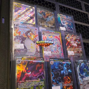 May include: A collection of eight Pok&eacute;mon trading cards displayed in clear protective sleeves. The cards feature various characters including Charizard, Gengar, and Sylveon with colorful holographic artwork and text. A SolidState Print logo is visible.
