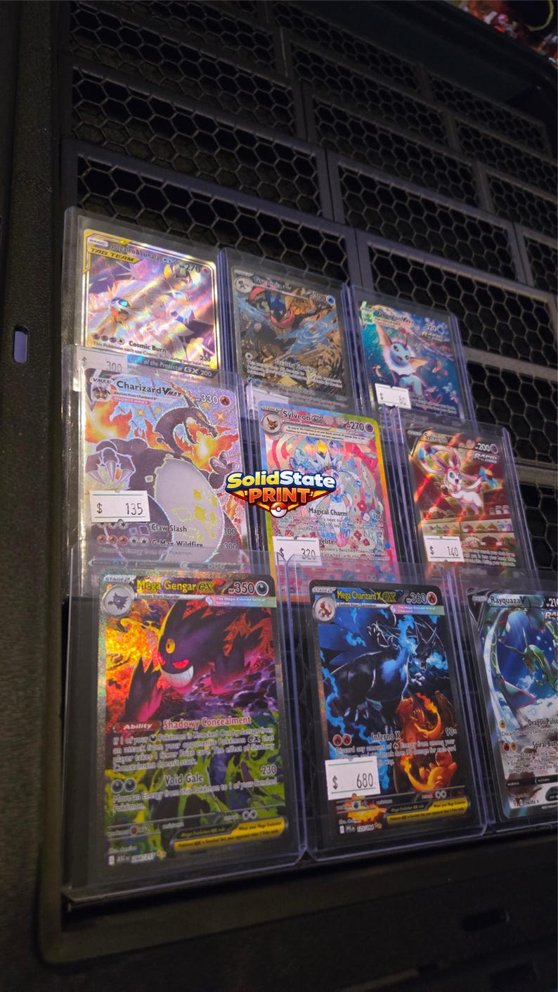 May include: A collection of eight Pok&eacute;mon trading cards displayed in clear protective sleeves. The cards feature various characters including Charizard, Gengar, and Sylveon with colorful holographic artwork and text. A SolidState Print logo is visible.