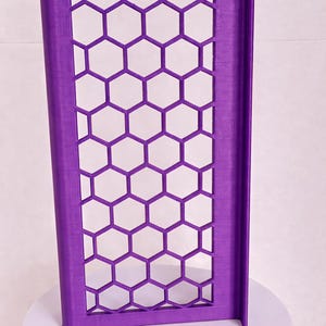 May include: A rectangular purple panel featuring a repeating honeycomb pattern of open hexagonal cutouts. The panel has a solid frame and a vertical edge flange on the right side, constructed with a visible layered texture throughout the surface.