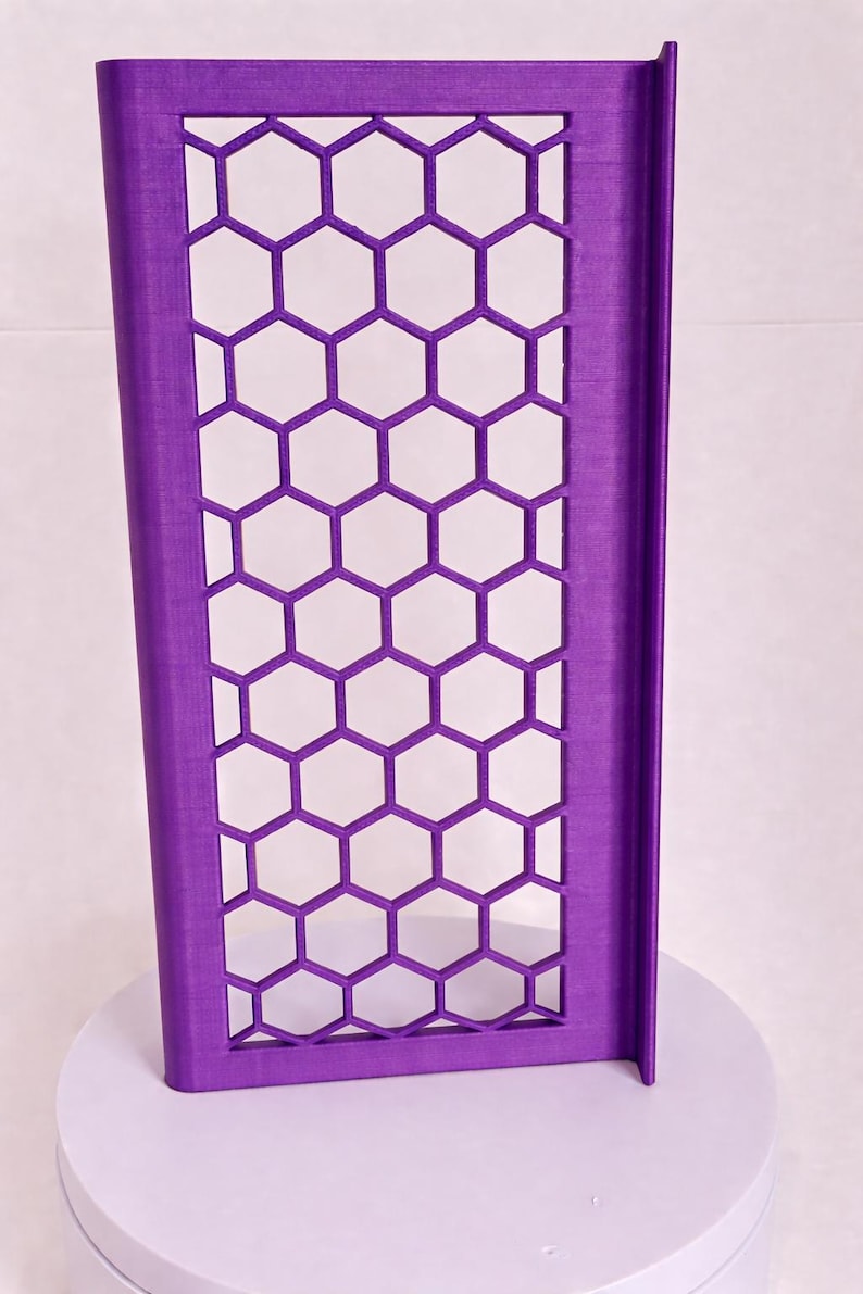 May include: A rectangular purple panel featuring a repeating honeycomb pattern of open hexagonal cutouts. The panel has a solid frame and a vertical edge flange on the right side, constructed with a visible layered texture throughout the surface.