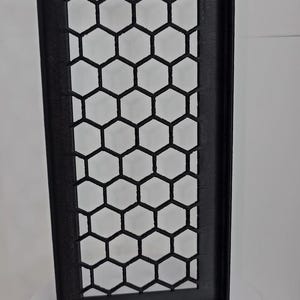 May include: A rectangular black panel featuring a repeating honeycomb pattern of hexagonal cutouts. The panel has a solid frame and a perpendicular flange extending along one of its long vertical edges, creating an L-shaped profile.