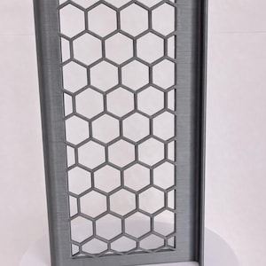 May include: A rectangular, dark gray panel featuring a repeating honeycomb lattice pattern. The structure has a solid frame with a vertical edge flange on the right side, displaying a textured surface finish consistent with 3D printed objects.