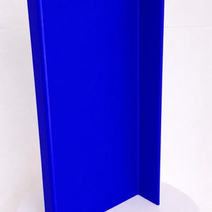 May include: A tall, vibrant blue vertical panel with a smooth, matte finish. The object features a distinct L-shaped profile, consisting of one wide front-facing section and a narrower side section, creating a sharp, clean right-angle corner.