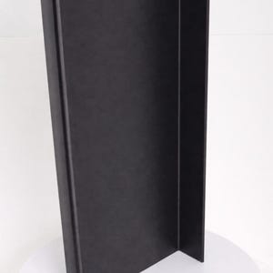 May include: A tall, matte black L-shaped display board featuring a smooth, solid surface. The structure consists of two rectangular panels joined at a right angle, standing vertically to provide a clean, dark backdrop for various items.