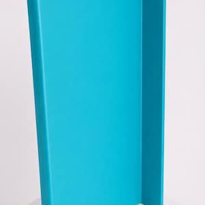 May include: A bright turquoise L-shaped panel with a smooth, matte finish. The object features a tall, vertical rectangular section connected to a shorter, perpendicular side panel, creating a clean, angular structure with rounded edges.