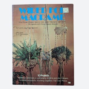 May include: A softcover craft book titled Wired for Macrame by Carole and Walter Pearson. The cover features three hanging macrame plant holders with green plants against a brown background, including text about 10 projects and knotting diagrams.