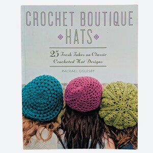May include: A softcover book titled Crochet Boutique Hats: 25 Fresh Takes on Classic Crocheted Hat Designs by Rachael Oglesby. The cover features three people wearing teal, magenta, and lime green crocheted hats with textured patterns.