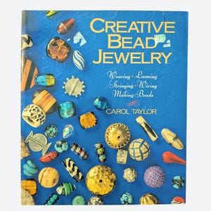 Może przedstawiać: Książka w twardej oprawie zatytułowana Creative Bead Jewelry autorstwa Carol Taylor z niebieską okładką przedstawiającą różne kolorowe koraliki. Podtytuł brzmi Weaving, Looming, Stringing, Wiring, Making Beads. Okładka pokazuje koraliki.