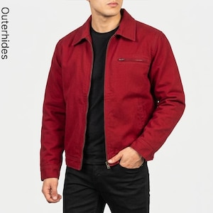 May include: A deep red zip-up jacket featuring a classic collar, long sleeves, and a horizontal zippered chest pocket. The garment is worn over a plain black t-shirt and black trousers. The text Outerhides is visible on the left side.