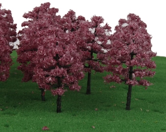 May include: A set of miniature model trees with dark brown trunks and pink foliage. The trees are arranged on a green grassy surface.
