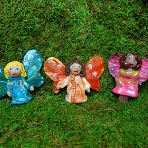 May include: Three handmade fairy figurines with wings. The fairies are made of polymer clay and have painted faces. The wings are painted in shades of blue, orange, and pink.