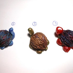 May include: Three small turtle figurines made from walnut shells. The turtles are painted in blue, gold, and red with glitter accents.