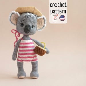 May include: A handmade crochet koala doll wearing a pink and white striped swimsuit and a tan hat. The koala holds a small brown basket with a yellow handle. The image includes the text "crochet pattern".
