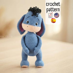 Könnte beinhalten: Ein handgefertigtes, blaues Häkeltier in Form eines Esels mit schwarzen Haaren und rosa gefütterten Ohren. Das Spielzeug hat eine beige Schnauze und steht auf seinen Hinterbeinen. Das Bild enthält den Text "crochet pattern" mit Flaggen.