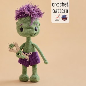 May include: A green crocheted doll with messy purple hair, wearing purple shorts and holding a small beige slingshot. The doll has black button eyes and a stitched smile. A white rectangular label displays the text crochet pattern.