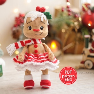 Peut inclure: Une poupée en pain d'épice crochetée au corps beige, portant une écharpe rayée rouge et blanche, une jupe à volants assortie et des bottes rouges. La poupée présente un détail de glaçage blanc sur la tête avec une baie rouge et deux boutons rouges.