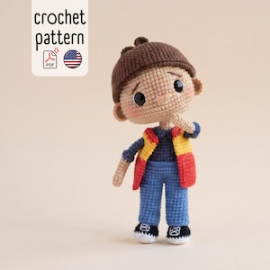Könnte beinhalten: Handgefertigte Häkelpuppe eines Jungen mit brauner Mütze, blauer Jeans, einem marineblauen Hemd und einer rot-gelben Weste. Die Puppe hat schwarze Turnschuhe und rosige Wangen. Das Bild enthält den Text "crochet pattern".